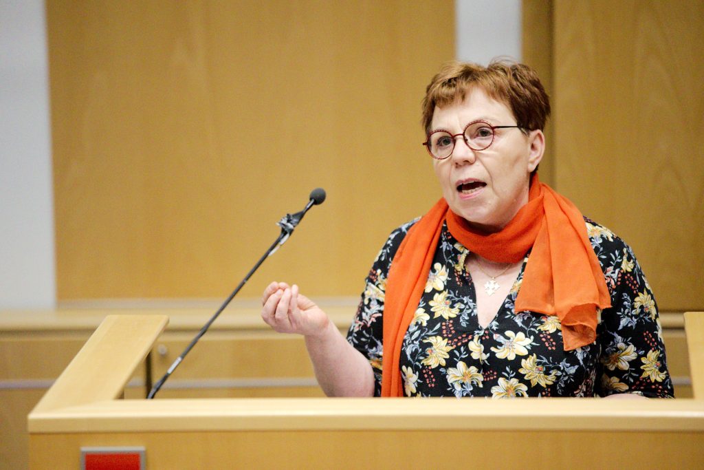 Merja Mäkisalo-Ropponen räsikyvän oranssissa huivissaan puhumassa puhujanpöntössä.